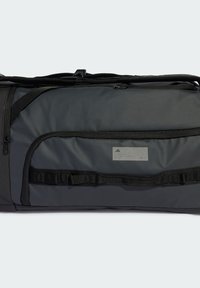 Crna torba s jastučićima s teksturiranom površinom, gornjim zatvaračem, prednjim džepom sa zatvaračem i podesivim trakama. Ima logotip i oznaku.