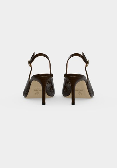 Paire de chaussures à talons hauts marron foncé avec brides arrière, bouts pointus et lanières à la cheville, vues de dos sur un fond clair uni.