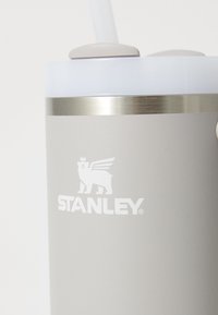Sivi izolirani spremnik za piće s nehrđajućim čeličnim pojasom, prozirnim poklopcem i slamkom. Sadrži "Stanley" logo u bijeloj boji.