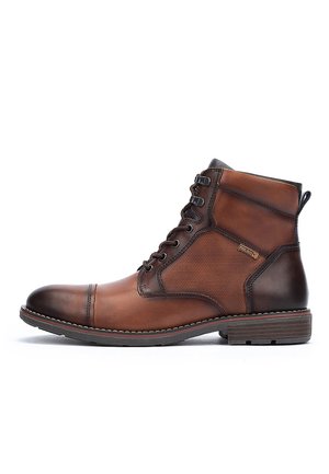 Bota de hombre de ante y cuero marrón con cordones, detalles de costura, tacón bajo y logo de la marca en el lateral.