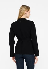Sort bæltejakke med krave, strukturerede skuldre og lange ærmer. Glat tekstur med et rent, minimalistisk design.