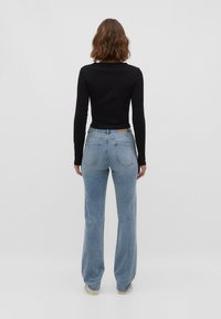 Černý přiléhavý top s dlouhým rukávem v kombinaci se světle modrými zvonovými džíny. Džíny mají klasický design s pěti kapsami a hnědou značkovou visačkou na pase.