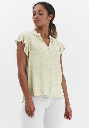 Lys grøn kortærmet bluse med volangkanter og knaplukning, prydet med blomster mønstre i gul og lilla, lavet af blødt stof.
