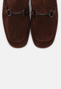 Mocassins en suède marron avec une surface lisse, un embout arrondi et des accents en métal noir décoratifs sur le cou-de-pied.