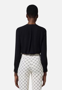 Blusa negra de mangas largas, con un pliegue en la parte posterior y detalles de corte en los puños, acompañada de pantalones blancos con estampado.