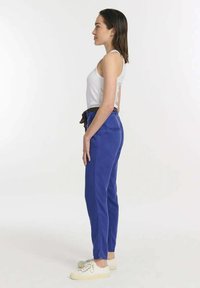 Blauwe katoenen broek met een trekkoord in de taille en twee zijzakken, gecombineerd met een witte tanktop en witte espadrilles.