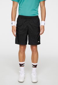 Svarta lätta shorts med elastisk midja, kombinerade med vita strumpor med ett färgglatt geometriskt mönster och vita sneakers.