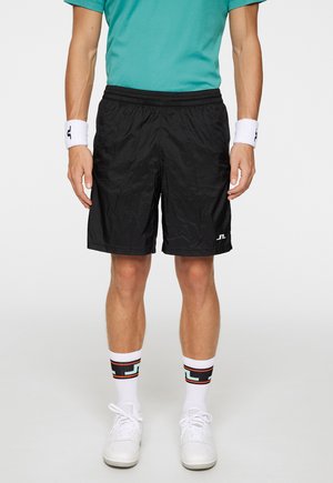 Sorte letvægts shorts med elastisk talje, kombineret med hvide strømper med et farverigt geometrisk mønster og hvide sneakers.