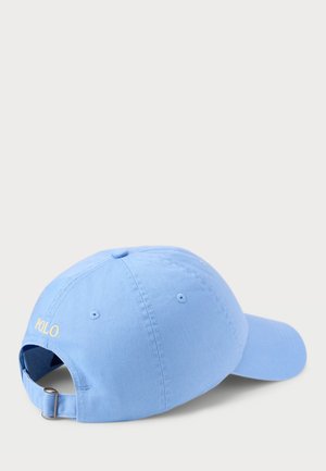 Šviesiai mėlyna medvilninė beisbolo kepurė su reguliuojamu dirželiu; gale siuvinėtas geltonos spalvos „POLO“ logotipas ir skylutės ventiliacijai.