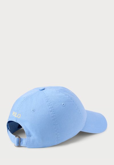 Světle modrá bavlněná baseballová čepice s nastavitelným páskem; vzadu má žlutě vyšitý nápis "POLO" a otvory pro větrání.