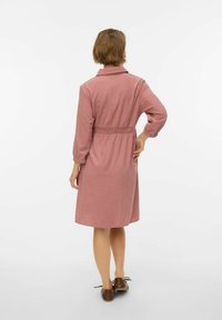 Obleka rožnate barve iz teksturirane tkanine z oprijatim pasom, dolgimi rokavi in ovratnikom. Srednje dolga z ravnim robom.