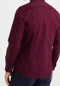 Burgundy långärmad skjorta med en strukturerad krage, knappmanschetter och en slät textur. Skuren i ryggen med en rundad nederkant.