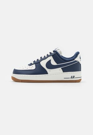 Baskets basses en cuir blanc et bleu marine, lacets blancs, semelle en gomme et logo Nike bleu marine sur le côté.