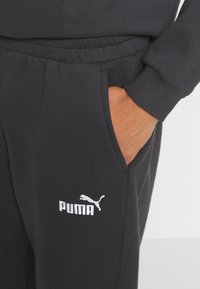 Pantalones de chándal negros de mezcla de algodón, con un logo blanco de Puma en el muslo izquierdo y puños y cintura acanalados. Con bolsillos en los lados.