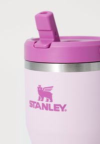 Pink stainless steel tumbler with a purple lid, featuring a straw opening and a logo of a winged bear, smooth texture.