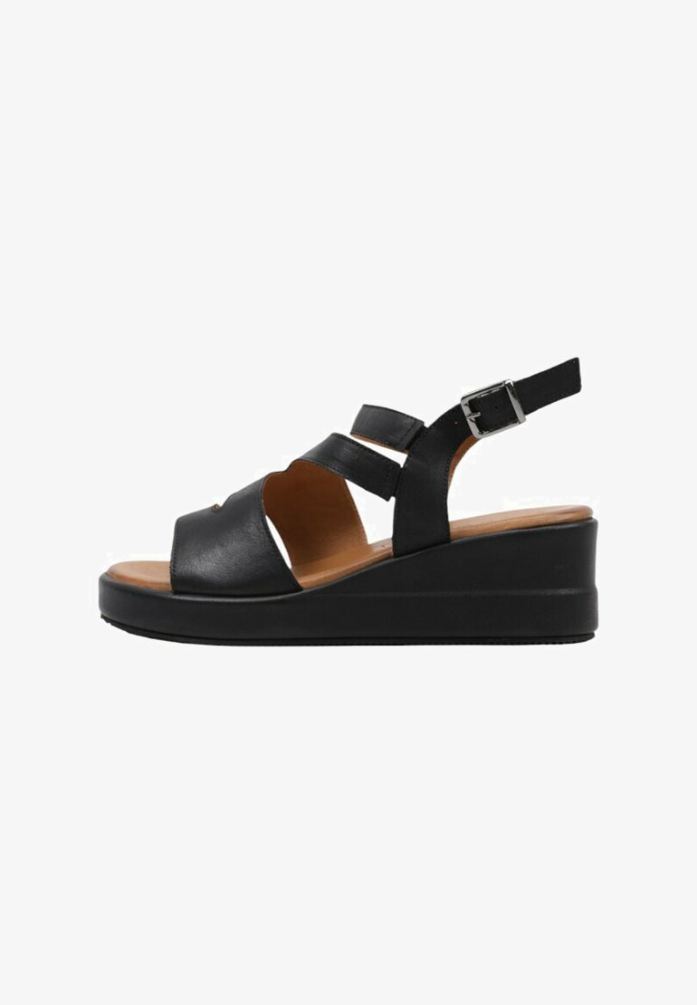 Sandalias de cuña de cuero negro con dos tiras frontales, correa ajustable en el tobillo y suela de goma texturizada. Plantilla marrón visible.