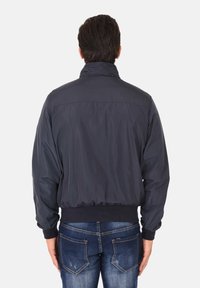 Giacca bomber blu navy con colletto alto, polsini e vita elasticizzati. Realizzata in tessuto leggero e liscio con una finitura leggermente lucida.
