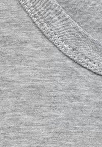 Szara bawełniana tkanina o gładkiej fakturze z subtelnym wzorem melanżowym. Widoczne szwy przy dekolcie podkreślają trwałość.