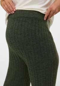 Dark green ribbed knit leggings with a high waistband, showcasing a soft texture and subtle color variation. Close-up view of fabric details.