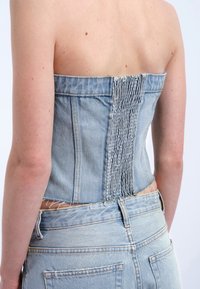Denim strapless topp med en figursydd design, featuring ett rynkat backstycke, ljusblå färg och fransad nederkant. Matchas med jeans i samma stil.