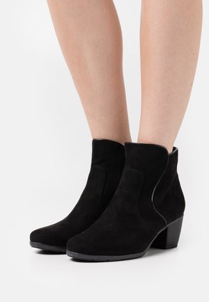 Schwarze Wildleder-Stiefeletten mit niedrigem Blockabsatz, die ein einfaches Design und geschwungene Seitenausschnitte aufweisen und eine glatte Textur präsentieren.