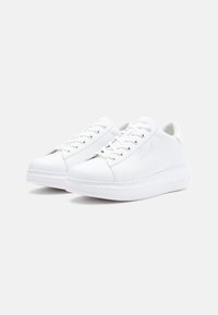 White sneakers made of synthetic material with round toes, lace-up design, and a thick sole featuring embossed branding on the side.