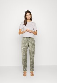T-shirt de mangas curtas lilás claro, combinado com calças largas verdes-oliva com um padrão texturizado branco e faixa elástica na cintura. Sandálias amarelas de tiras.