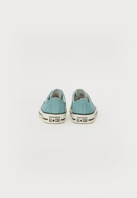 Light blue canvas sneakers with a low-top design, white rubber soles, and black accents. Features a logo on the heel.
