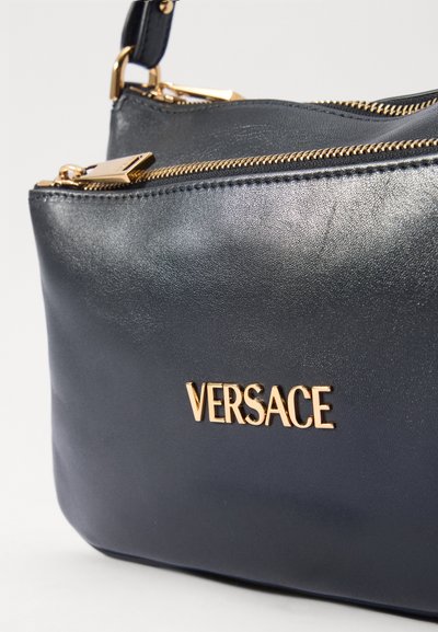 Borsa a tracolla in pelle nera con zip e accessori in tonalità oro, con la scritta "VERSACE" impresso sul davanti. Texture liscia e forma compatta.