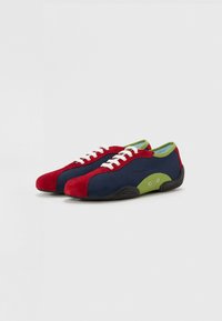 Zapatos de ante en colores rojo, azul marino y verde. Diseño de perfil bajo con cordones blancos y suela de goma. Detalles de costura y acentos laterales notables.