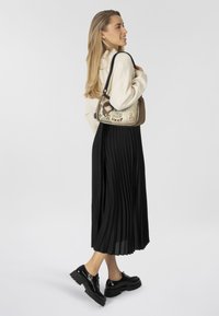 Faltenrock in Schwarz, cremeweißes Sweatshirt und glänzende schwarze Plateauschuhe. Die Handtasche zeigt ein Cartoon-Design mit dem Text "Be Yourself".