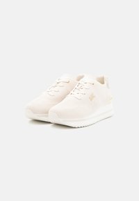 White knitted sneakers with a textured surface, flat laces, and gold accents on the heel. Features a cushioned, ridged sole.