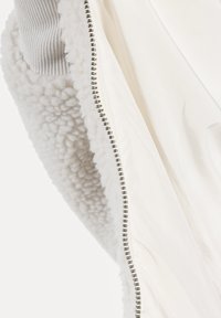 Chaqueta blanca con un interior de felpa suave y esponjoso, un exterior liso y una cremallera plateada en la costura, con puños acanalados grises.