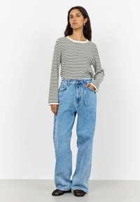 Gestreiftes Langarmoberteil aus weißer und schwarzer Baumwolle, kombiniert mit locker sitzenden hellblauen Denim-Jeans mit Kordelzugbund und Taschen.