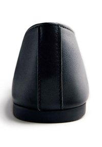 Zapato de cuero negro exhibido desde la parte trasera, con un acabado suave, tacón redondeado y detalles de costura sutiles a lo largo de los lados.