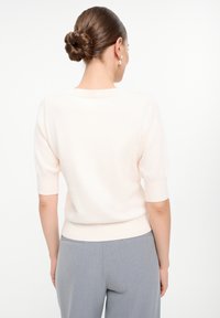 Jasno brzoskwiniowy sweter z krótkim rękawem, okrągłym dekoltem i ściągaczem u dołu, zestawiony z szarymi spodniami. Gładka tekstura, prosty design.