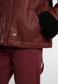 Bordeaux, getextureerde jas met een zwart nepleren kraag, voorzien van een knopenfrontsluiting en zijvakken, gecombineerd met bijpassende bordeauxkleurige broek.