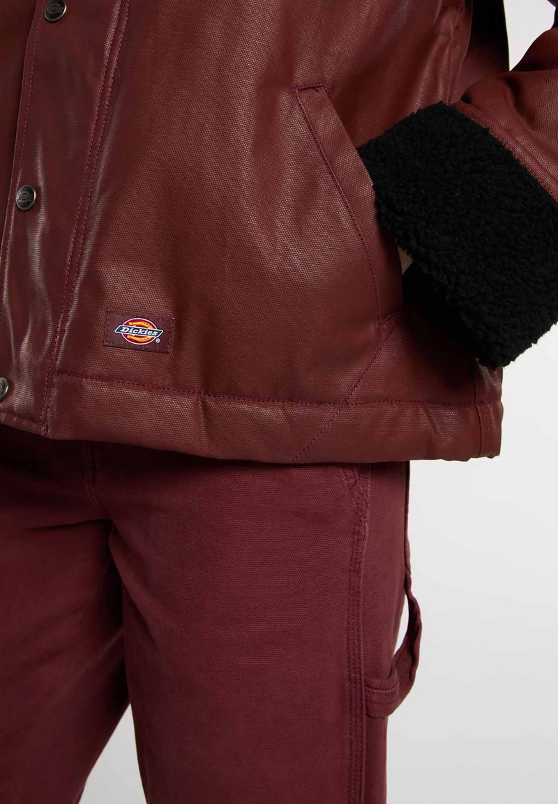 Giacca bordeaux con trama, dotata di colletto in pelliccia sintetica nera, caratterizzata da chiusura frontale con bottoni e tasche laterali, abbinata a pantaloni bordeaux coordinati.
