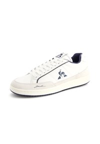 Vit sneaker med marinblå detaljer, med en mocka tåkappa, platta snören och en texturerad gummisula. Logotypdetalj på sidan.