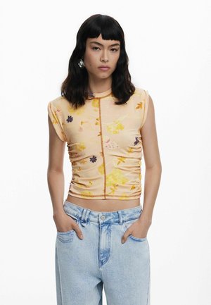 Hedvábný krémový crop top s květinovým potiskem a poloprůhledným materiálem, s nařaseným designem a krátkými rukávy; doplněný o světle modré džíny s vysokým pasem.