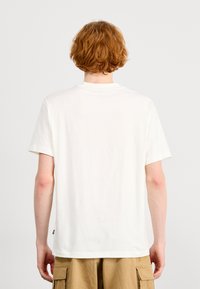 Camisa de algodón blanca con mangas cortas, cuello redondo y un diseño recto. Sin gráficos ni patrones visibles, textura suave.
