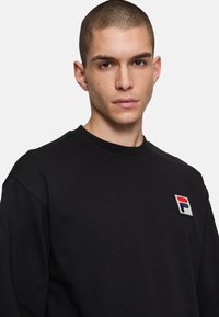 Felpa nera, in misto cotone, con colletto a girocollo ribbed, presenta un piccolo logo ricamato in rosso, bianco e blu sul petto.