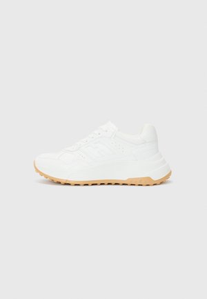 White athletic sneaker with a textured upper, padded collar, and a beige rubber sole featuring a patterned tread. Contains lace closure.