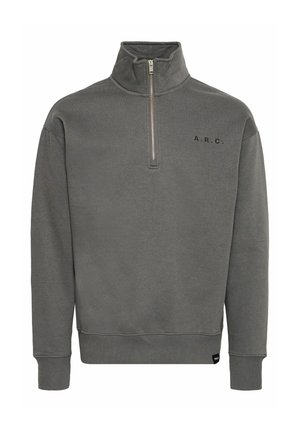 Pelēka augsto apkakli ar rāvējslēdzēju, pirmajā rāvējslēdzēja pusē, ar ribotām piedurknēm un melnu tekstu "A.R.C." uz krūtīm. Mīksta auduma tekstūra.