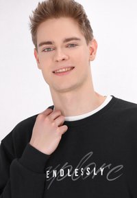 Hanorac negru cu text gri și alb "ENDLESSLY", mâneci cu țesătură elastică și guler alb rotund. Textură netedă și design casual.
