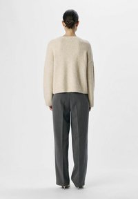 Un pull beige cropped en tissu doux et texturé, associé à un pantalon gris taille haute, présentant un design simple et décontracté vu de dos.