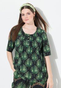 Černé tričko s potiskem zelených palm na kulatém výstřihu, krátkými rukávy a detailním zapínáním na knoflíky. Modelka má na sobě odpovídající zelenou čelenku.