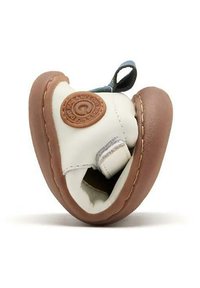 Zapato de cuero blanco con suela de goma marrón, diseño curvado, detalles cosidos y un parche con logo circular. Cuenta con un lazo para facilitar el agarre.