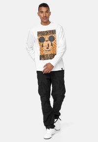 Hvid langærmet skjorte med sort og orange Mickey Mouse grafik. Bæres med sorte cargo bukser og hvide sneakers.