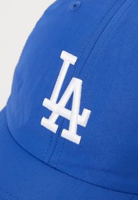 Modrá baseballová čiapka vyrobená z textílie, s bielou vyšitou „LA“ logom na prednej strane. Štruktúrovaný dizajn s zakriveným šiltom.